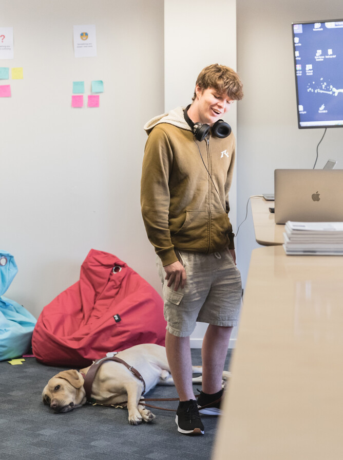 Lawson smiling next to his laptop, while his dog Aidan lies on the floor